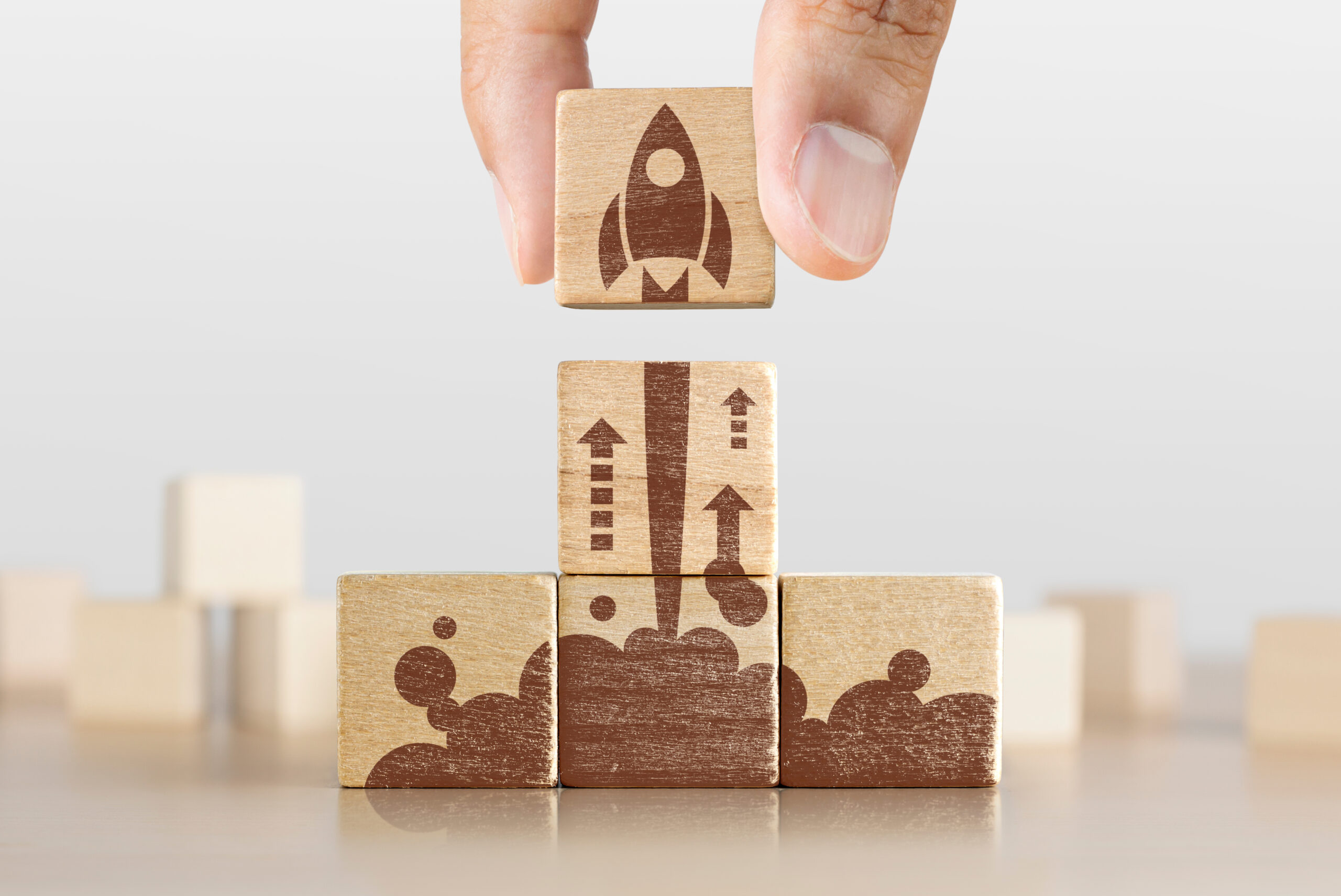 Wooden blocks with launching rocket graphic arranged in pyramid shape and a man is holding the top one.