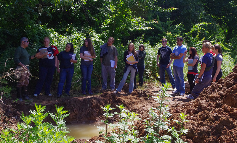 EPH Soils instructor Vinnie Agovino lectures to students outside next to a muddy soil pit