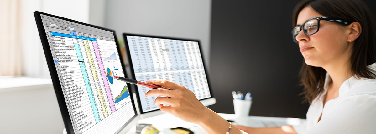 Woman pointing pen at computer screen showing spreadsheet and pie chart