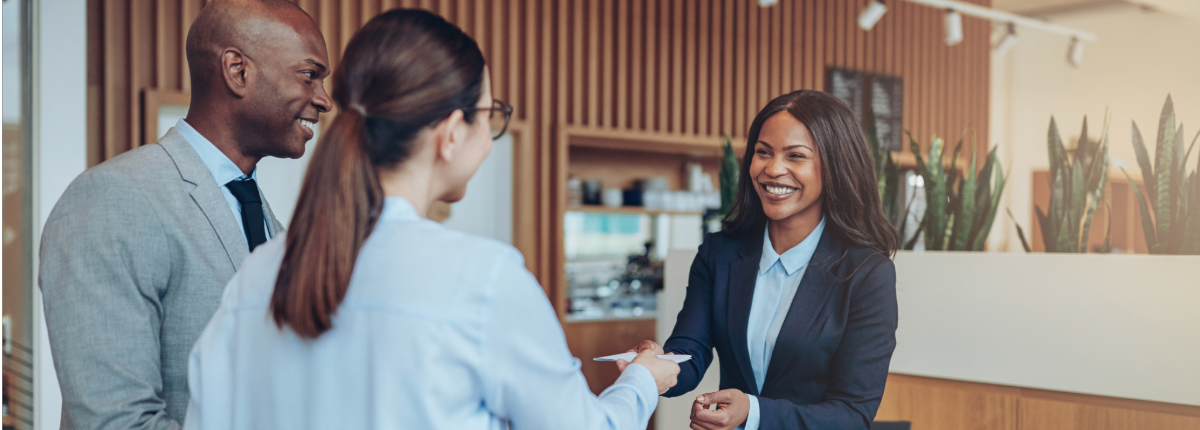 Two happy customers are helped by a smiling, attentive customer service professional
