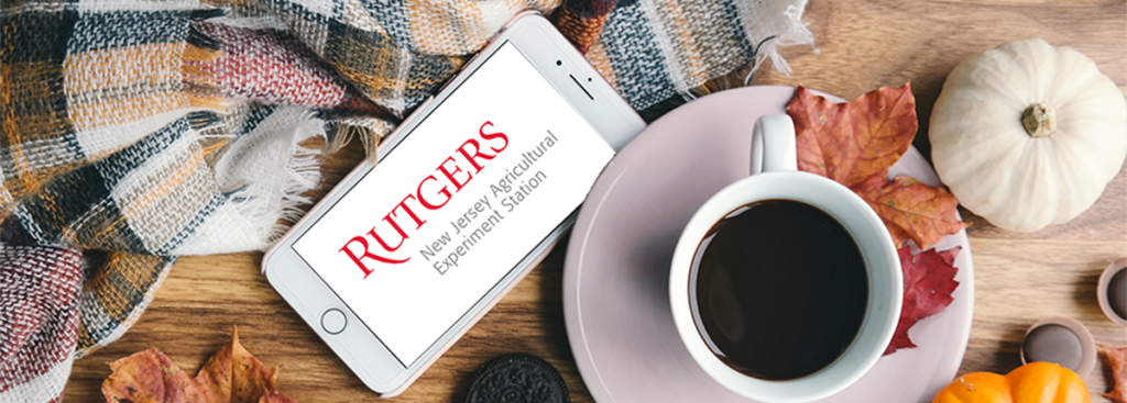 Cup of coffee surrounded by small pumpkins, fall leaves, scarf, and smarphone with Rutgers NJAES logo on the screen