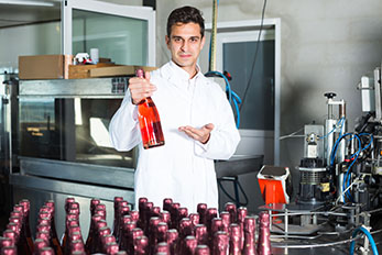 man working in wine production facility and holding up bottle of wine