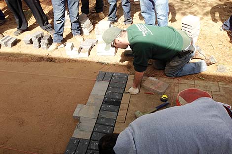Students watch as instructor Alex Burke lines up stones in a new paver walkway.