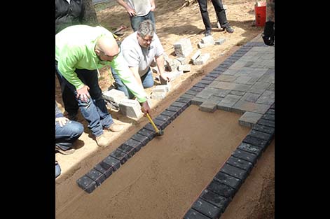 Thomas McAnany taps border stones back into alignment for a new paver walkway students are building in a hands-on landscaping course at Rutgers.
