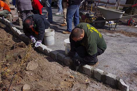 Students add mortar to a decorative paver wall