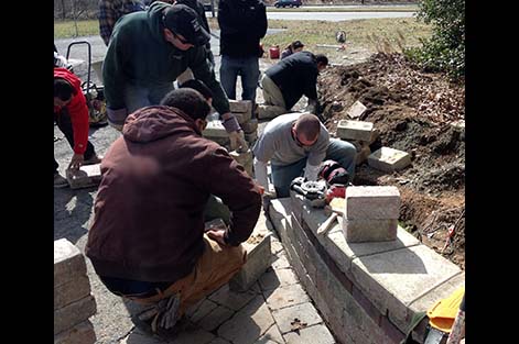 Students work together on building a decorative wall constructed with concrete pavers.