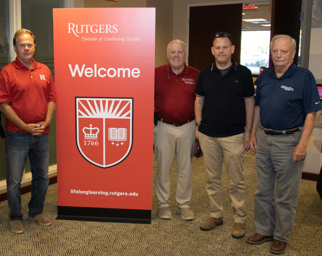 Members of the instructional team for the Rutgers Professional Golf Turf Management School standing by a welcome sign featuring the Rutgers shield