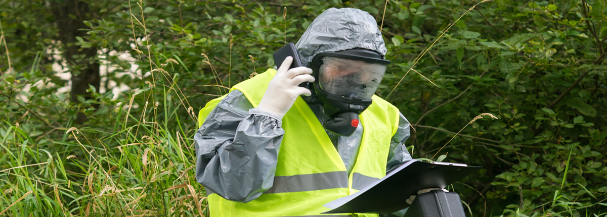 A person in a protective suit talks on the phone while looking at environmental study data on a clipboard