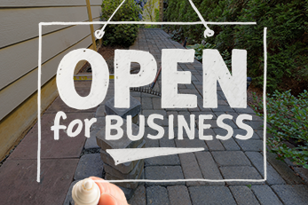 Open for Business sign overlayed over concrete paver walkway with shrubs on either side