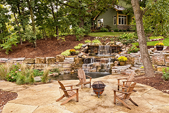 Beautifully landscaped backyard scene featuring a pond, waterfall, pavers, plants, and retaining walls