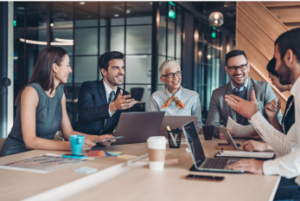 Image of an office team meeting around a table, smiling and talking