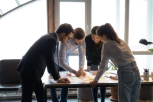 A group of professionals stands around a table looking at and working on documents