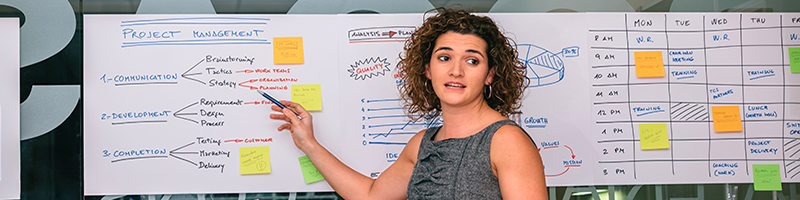 Female project manager pointing to charts hanging on glass wall