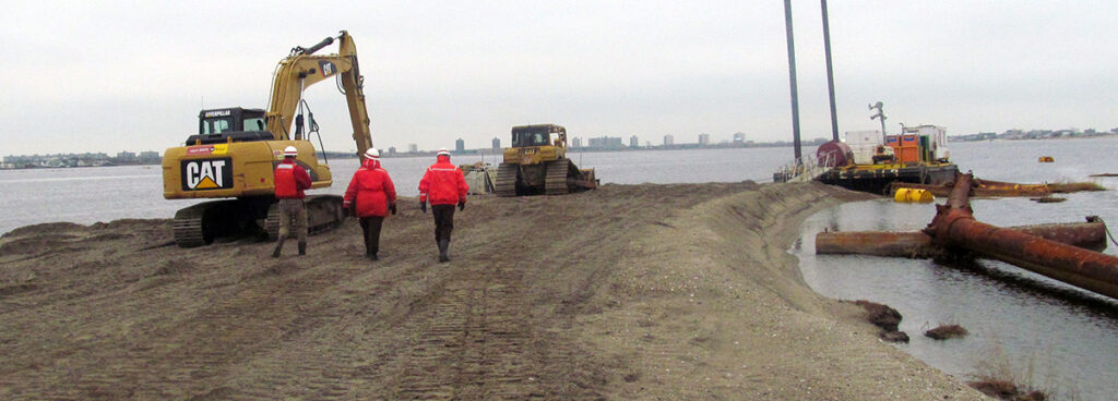 Environmental engineers walking toward construction vehicles working on recovery of degraded waterfront ecosystem