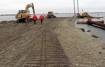 Environmental engineers walking toward construction vehicles working on recovery of degraded waterfront ecosystem