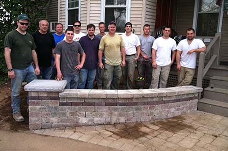 Students from the Concrete Pavers course stand behind the wall they completed for their hands-on project