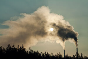 Two smokestacks silhouetted against sky with emissions obscuring the sun
