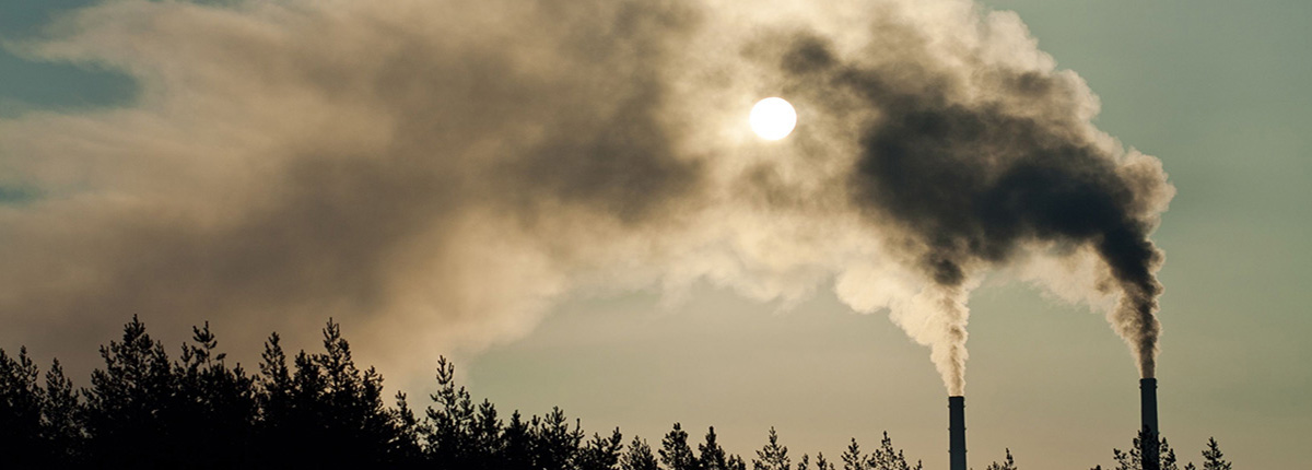 Two smokestacks silhouetted against sky with emissions obscuring the sun