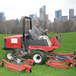 Central Park Conservancy staff on ride-on mower with NYC skyline in the background