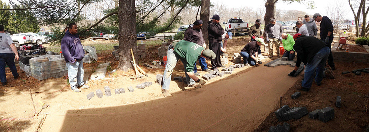 Instructor Alex Burke (dark green shirt) guides students as they lay pavers in a new walkway in this hands-on landscaping course at Rutgers.