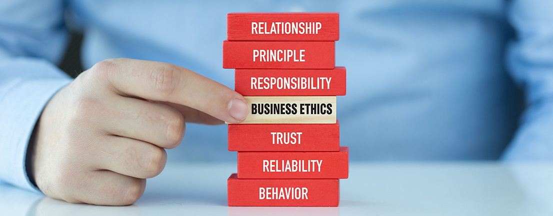 Hand inserting tan block reading Business Ethics into pile of red blocks with related terms on them such as responsibility, trust, and behavior