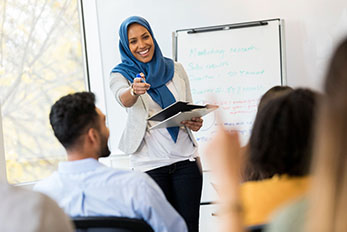 Muslim woman smiling and holding clipboard while giving presentation to colleagues