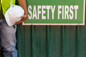 Hand holding safety helmet near sign reading Safety First
