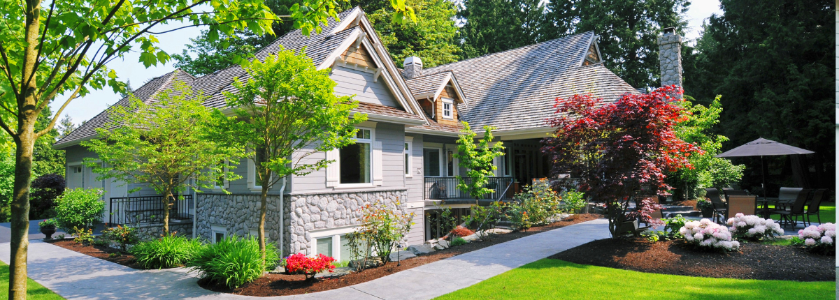 Image of a house with several garden beds containing a variety of attractive plants, flowers, and trees