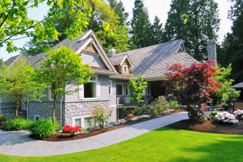 Image of a house with several garden beds containing a variety of attractive plants, flowers, and trees