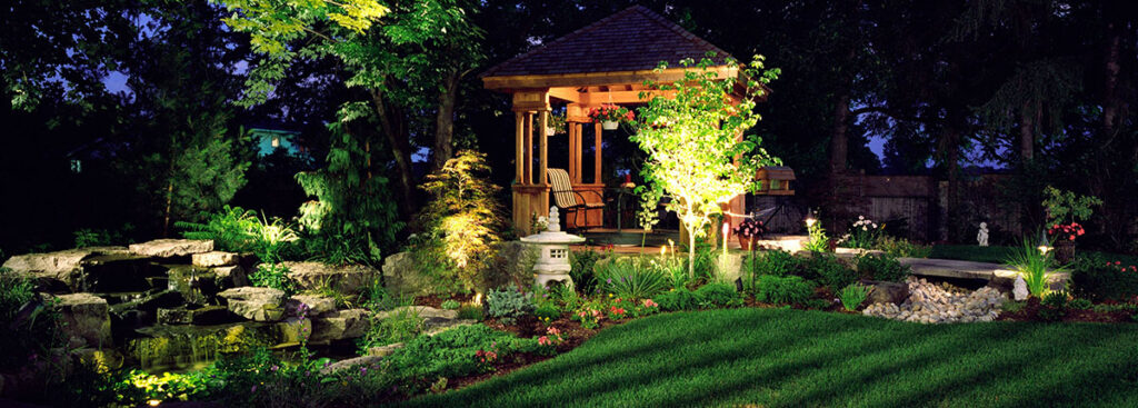 Beautiful garden with gazebo illuminated at night by landscape lighting