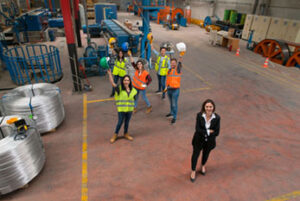Female supervisor standing in front of group of employees smiling and holding hard hats in the air