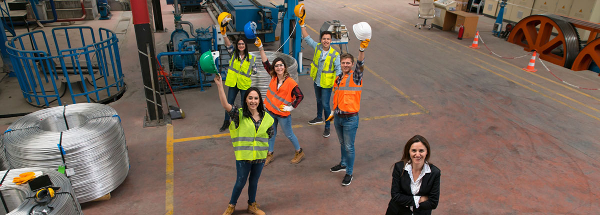 Female supervisor standing in front of group of employees smiling and holding hard hats in the air