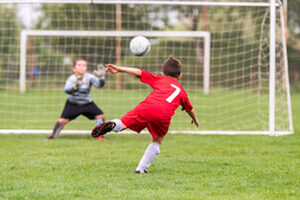 Boy kicking soccer ball toward net on grass field