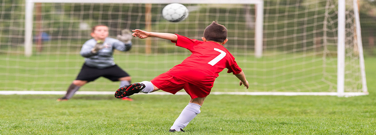 Boy kicking soccer ball toward net on grass field