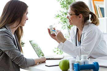 Female Dietician Holding Up Nutritional Supplement and Pointing to Label as she Talks to Patient