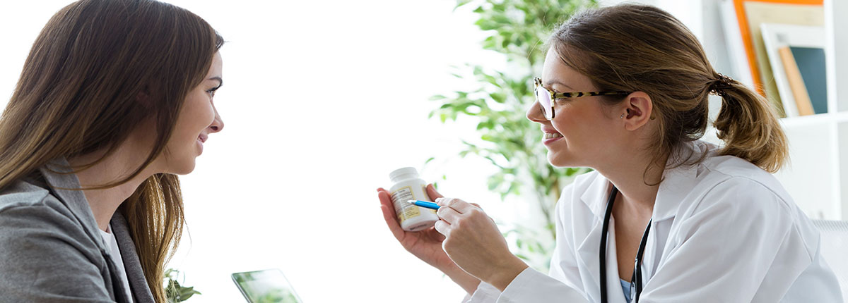 Female Dietician Holding Up Nutritional Supplement and Pointing to Label as she Talks to Patient