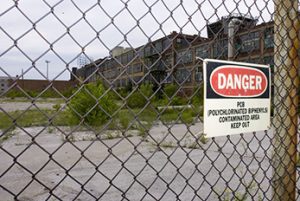 Sign warning of PCB contaminated area on chain link fence surrounding dilapidated building
