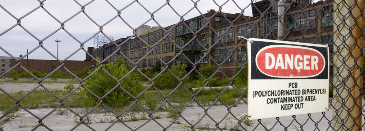 Sign warning of PCB contaminated area on chain link fence surrounding dilapidated building