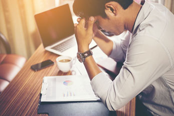 Man sitting at work desk and holding head in his hands