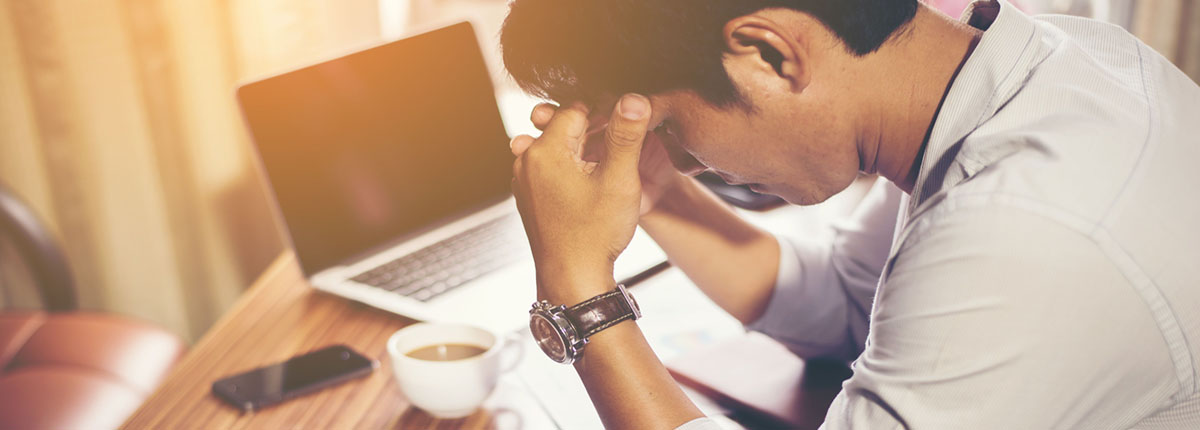 Man sitting at work desk and holding head in his hands