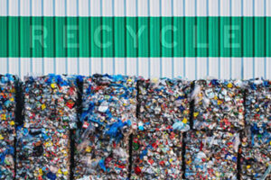 The word Recycle on corrugated metal wall above bales of plastic recyclables