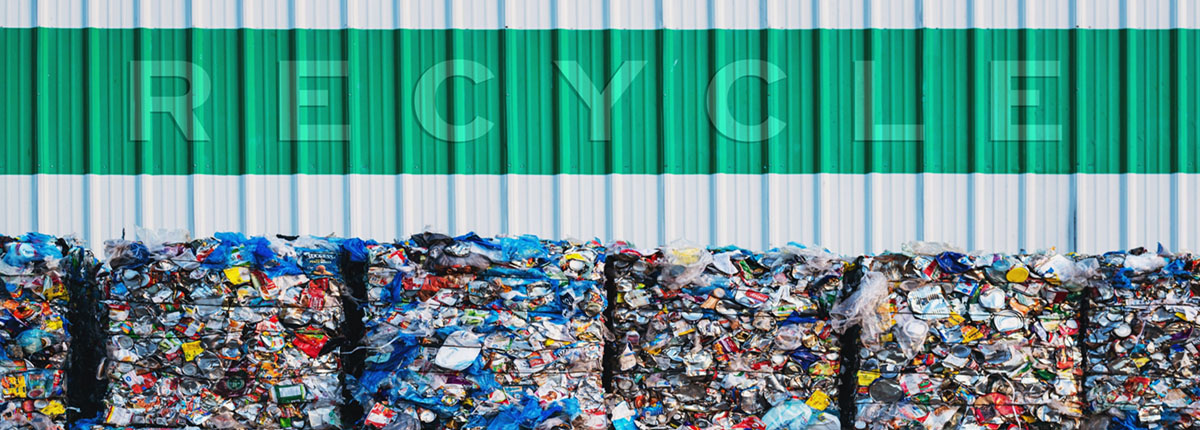 The word Recycle on corrugated metal wall above bales of plastic recyclables